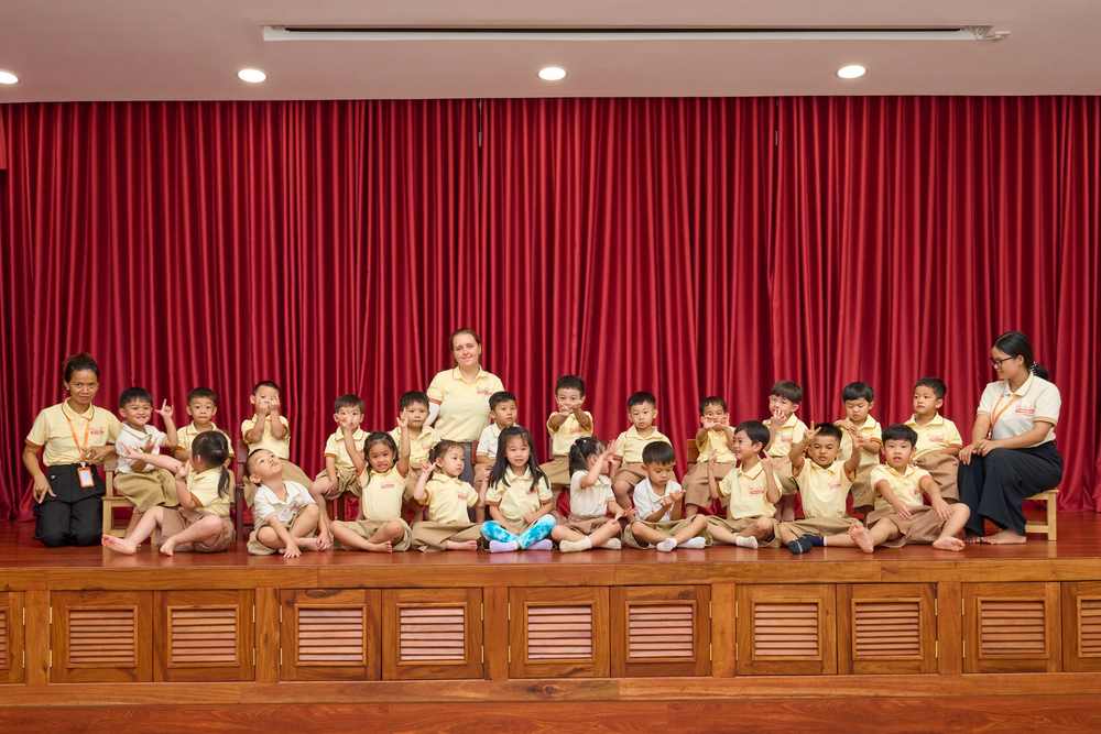 Giraffe Class, the largest group, seated in two rows on the hall stage with teachers at either end