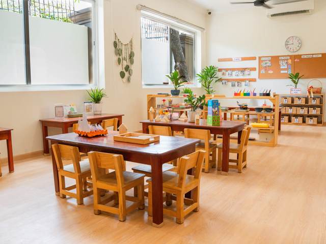 A classroom at Orange Crest Preschool with a low timber table and chairs and a shelf of wicker baskets beneath a pinboard