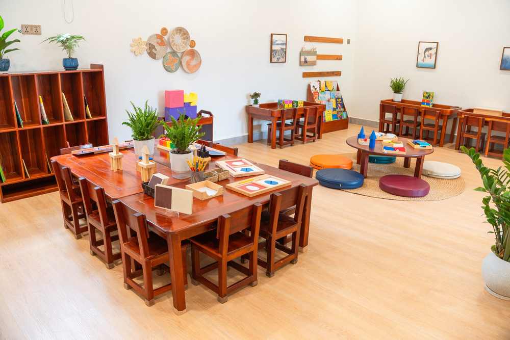 Timber tables and chairs in a classroom at Orange Crest Preschool, with a bookshelf and plants along the wall