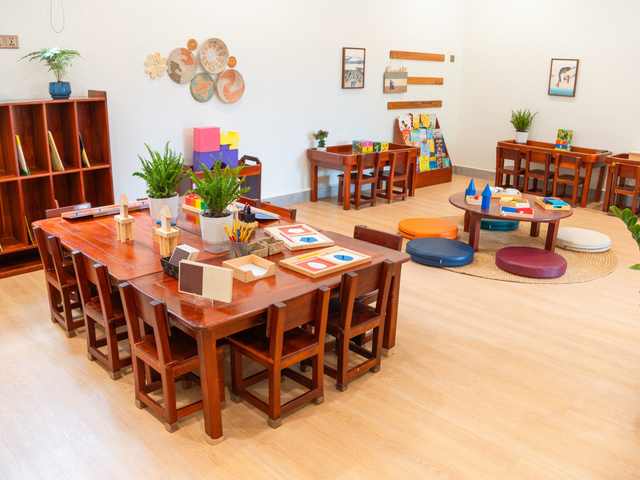 Timber tables and chairs in a classroom at Orange Crest Preschool, with a bookshelf and plants along the wall