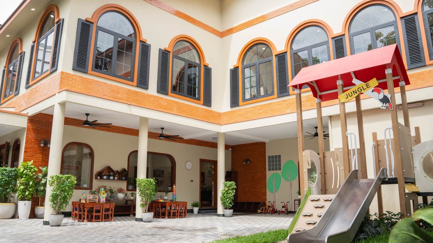 The Orange Crest Preschool courtyard after its 2026 renovation, with the playhouse and slide below two storeys of arched windows