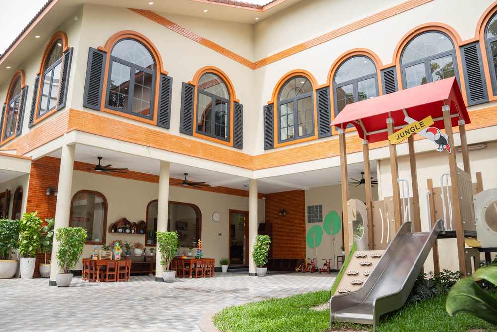 The courtyard at Orange Crest Preschool, with the playhouse and slide in the foreground and arched windows on both storeys of the building behind