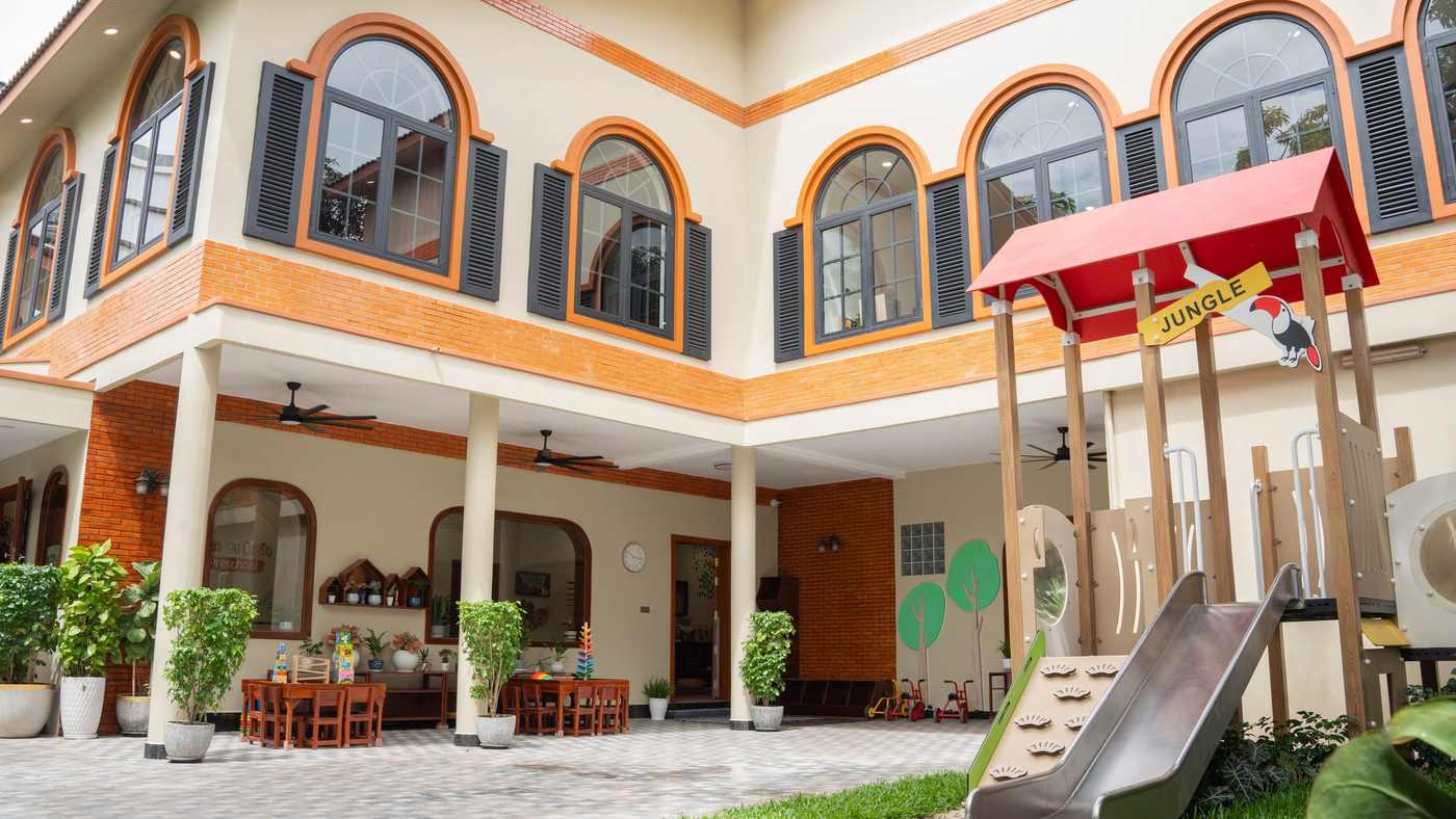 The Orange Crest Preschool courtyard after its 2026 renovation, with the playhouse and slide below two storeys of arched windows