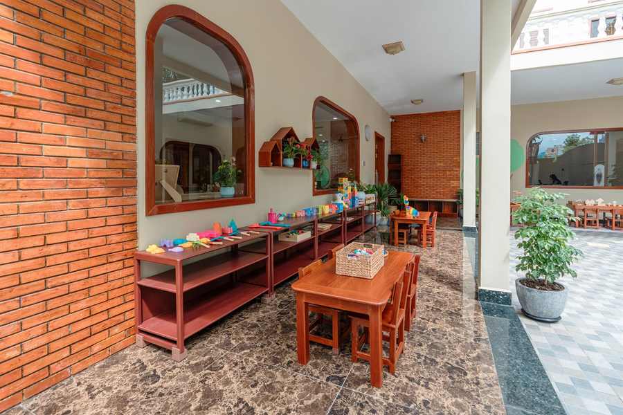 The covered brick arcade at Orange Crest Preschool, with low wooden tables set out along it