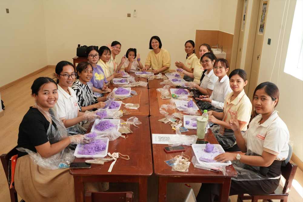 Teachers sitting along both sides of a long table, each working on a craft with purple modelling material laid out on trays