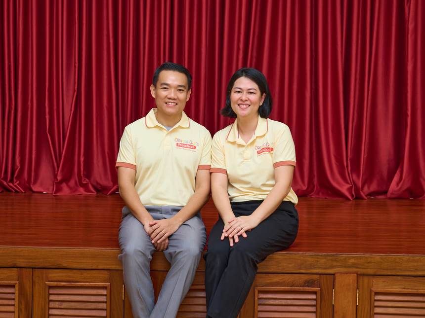 Keath Seng and Judy Zhang, Director and Principal of Orange Crest Preschool, seated together on the stage of the school hall