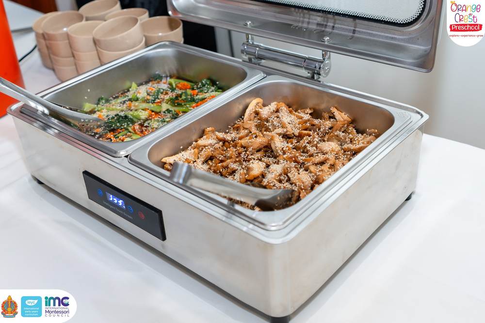 Two stainless steel warming trays holding stir-fried greens with carrot and a chicken dish