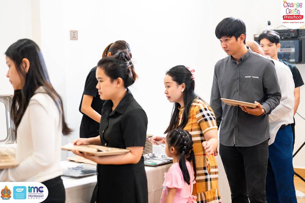Parents queueing at the serving table, each holding one of the compartment trays the children eat from