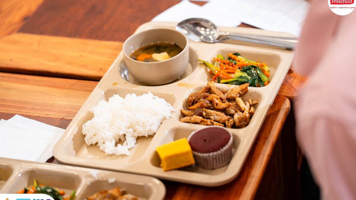 A kindergarten lunch tray at Orange Crest Preschool in Phnom Penh: rice, a chicken dish, stir-fried vegetables, steamed pumpkin, a bowl of soup and a small dessert