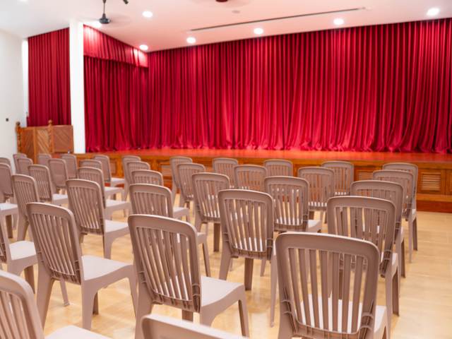 The hall at Orange Crest Preschool, with rows of chairs facing a stage hung with red curtains