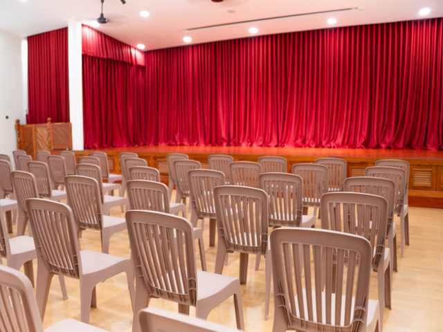 The hall at Orange Crest Preschool, with rows of chairs facing a stage hung with red curtains