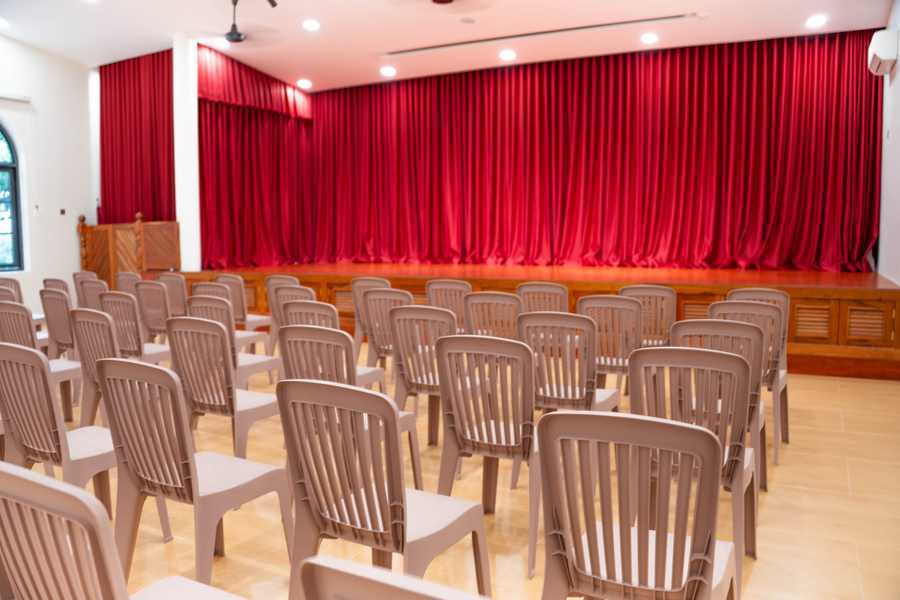 The hall at Orange Crest Preschool, with rows of chairs facing a stage hung with red curtains