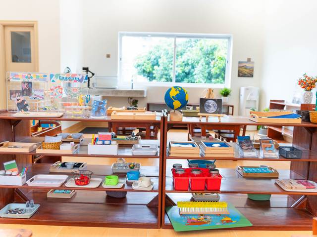 Trays and boxes of learning materials on open timber shelves at Orange Crest Preschool, with a globe on top