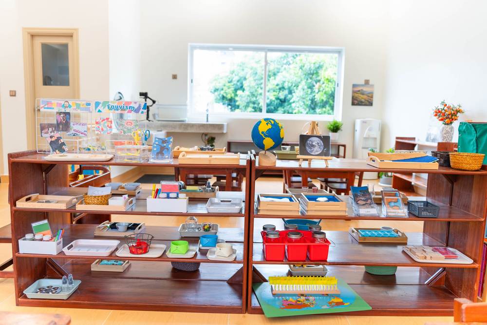 Montessori learning materials and a globe set out on a low wooden shelf in a classroom at Orange Crest Preschool