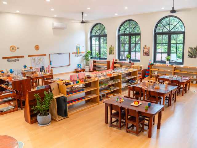 A Montessori classroom at Orange Crest Preschool, with low tables and open shelves beneath tall arched windows
