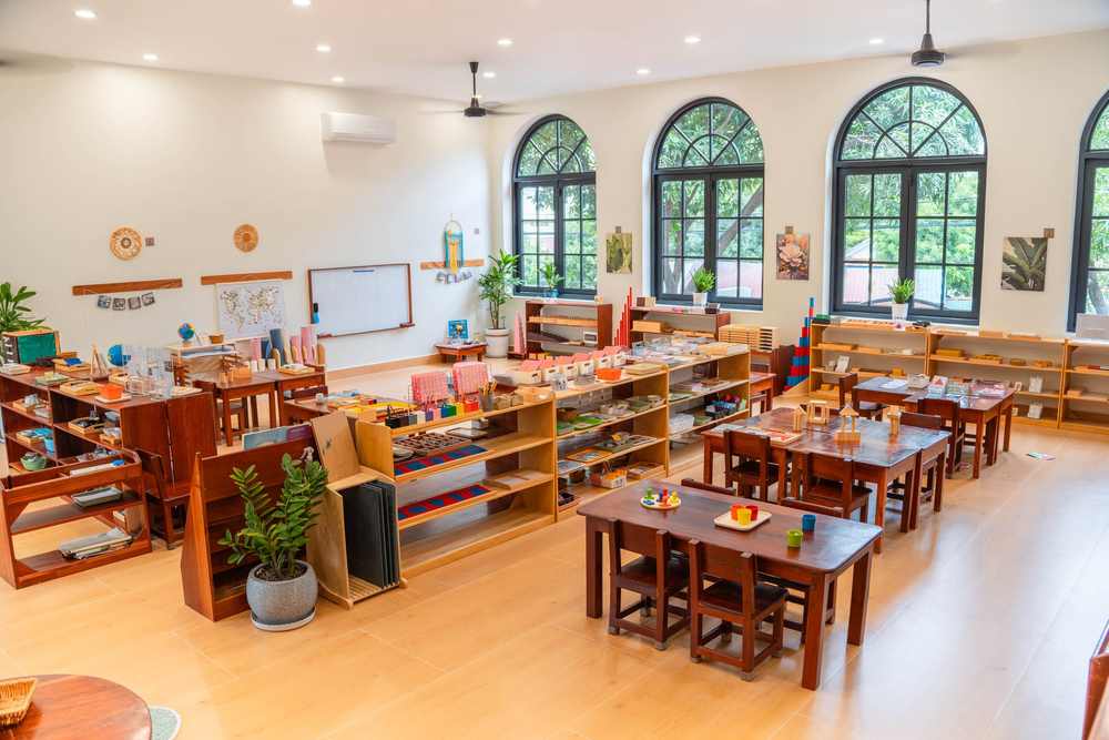 A Montessori classroom at Orange Crest Preschool, with low tables, open shelves and a row of tall arched windows