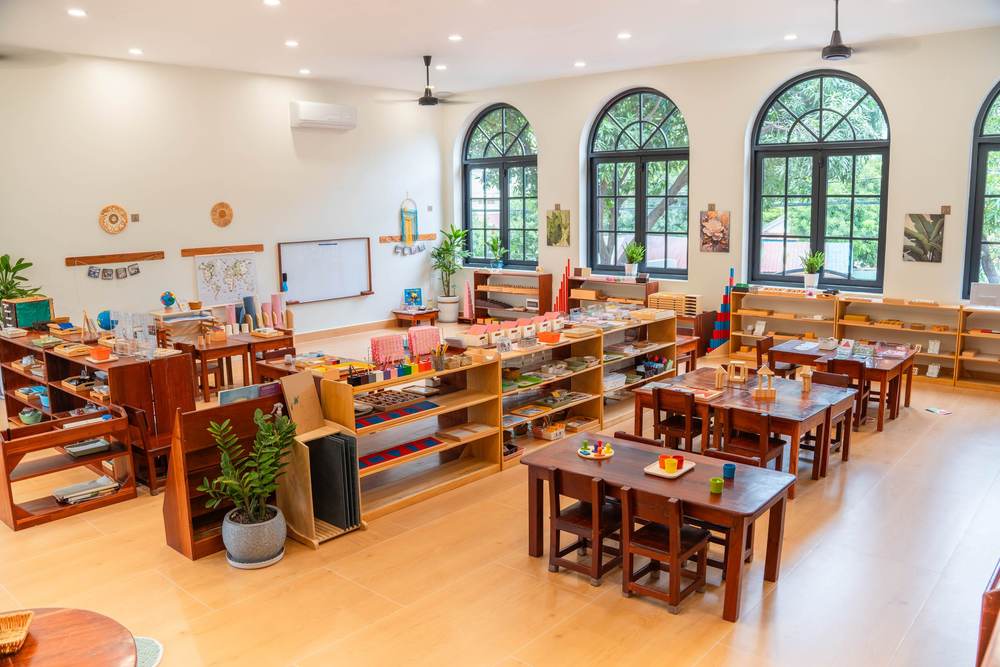 A Montessori classroom at Orange Crest Preschool, with low tables, open shelves and a row of tall arched windows