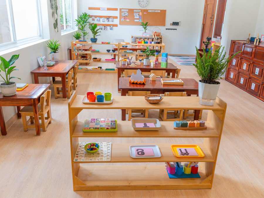 Montessori materials set out on trays on low open timber shelves in a classroom