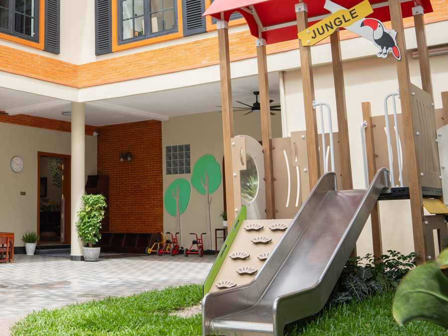 The playhouse, climbing frame and slide in the renovated courtyard of Orange Crest Preschool, beneath arched windows