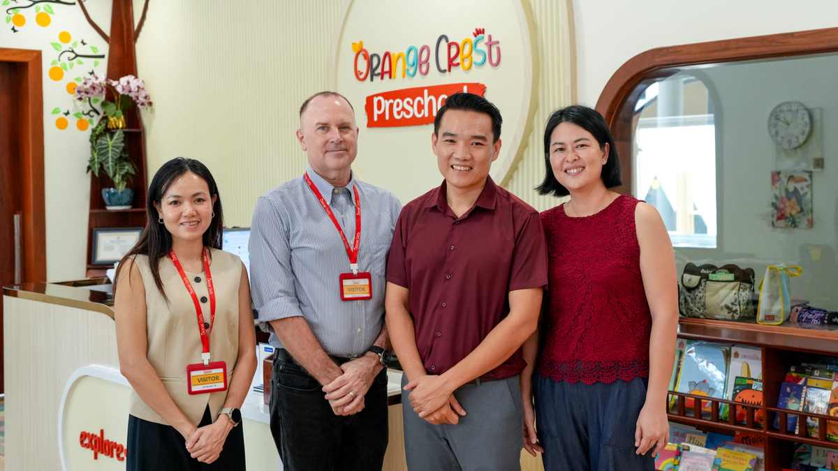 Four adults standing together at the reception desk at Orange Crest Preschool, beneath the round school sign