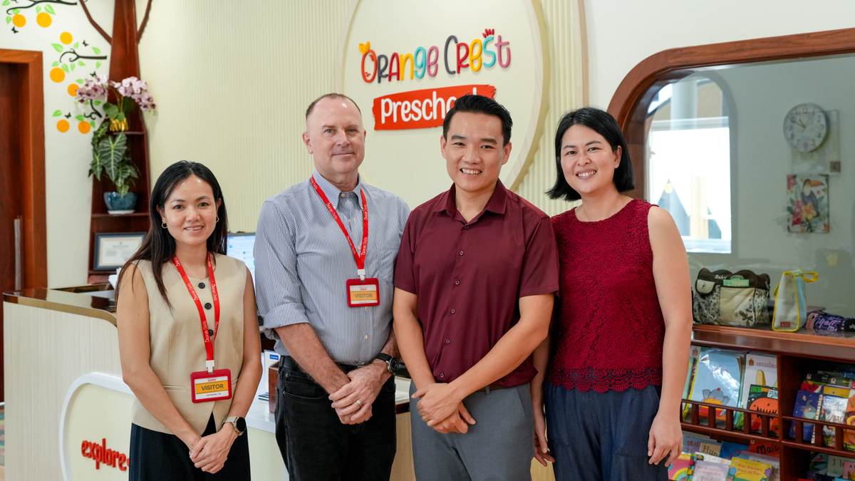 Four adults standing together at the reception desk at Orange Crest Preschool, beneath the round school sign