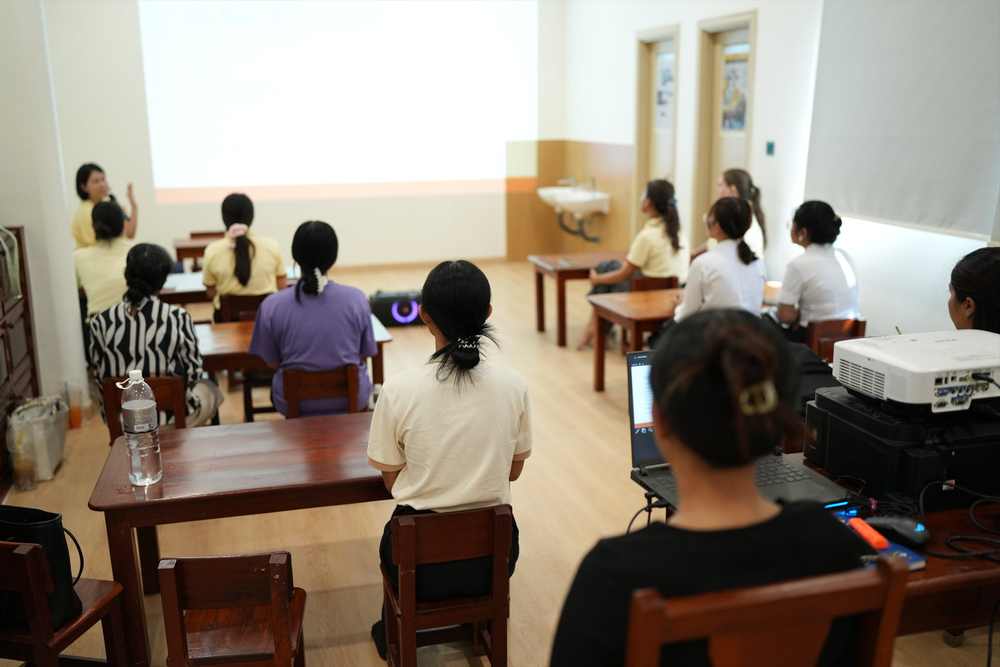 Teachers seated at tables in the training room, facing a projector screen during the orientation session