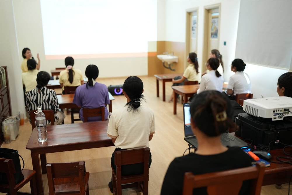 Teachers seated at tables in the training room, facing a projector screen during the orientation session