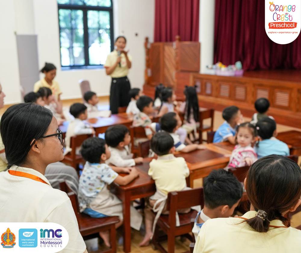 Children from across the school sitting on the hall floor and on benches, facing the screen and their teachers