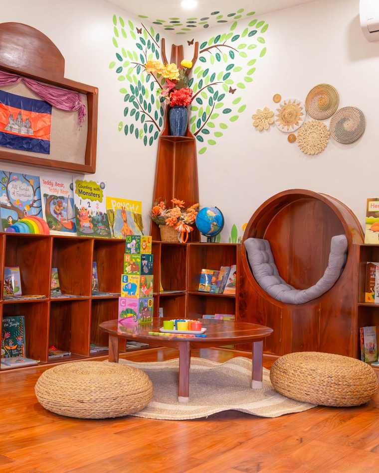 The reading nook at Orange Crest Preschool: a round timber seat beneath a painted tree, with low bookshelves and floor cushions