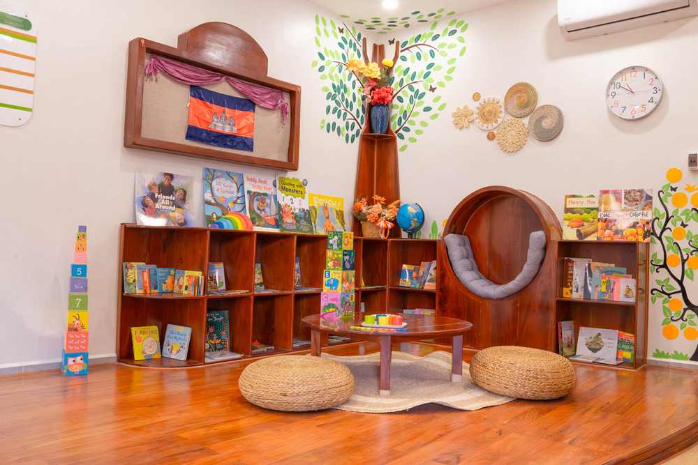 The reading nook at Orange Crest Preschool: a round timber seat beneath a painted tree, with low bookshelves and two floor cushions