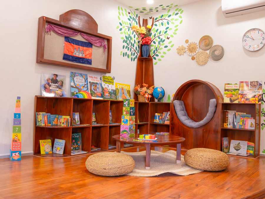 The reading nook at Orange Crest Preschool: a round timber seat beneath a painted tree, with low bookshelves and floor cushions
