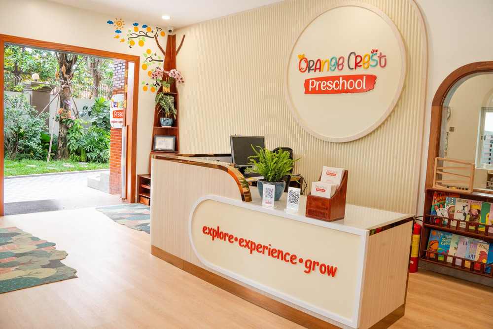 The reception desk at Orange Crest Preschool, with the round school sign on the wall behind it and the garden visible through the open door