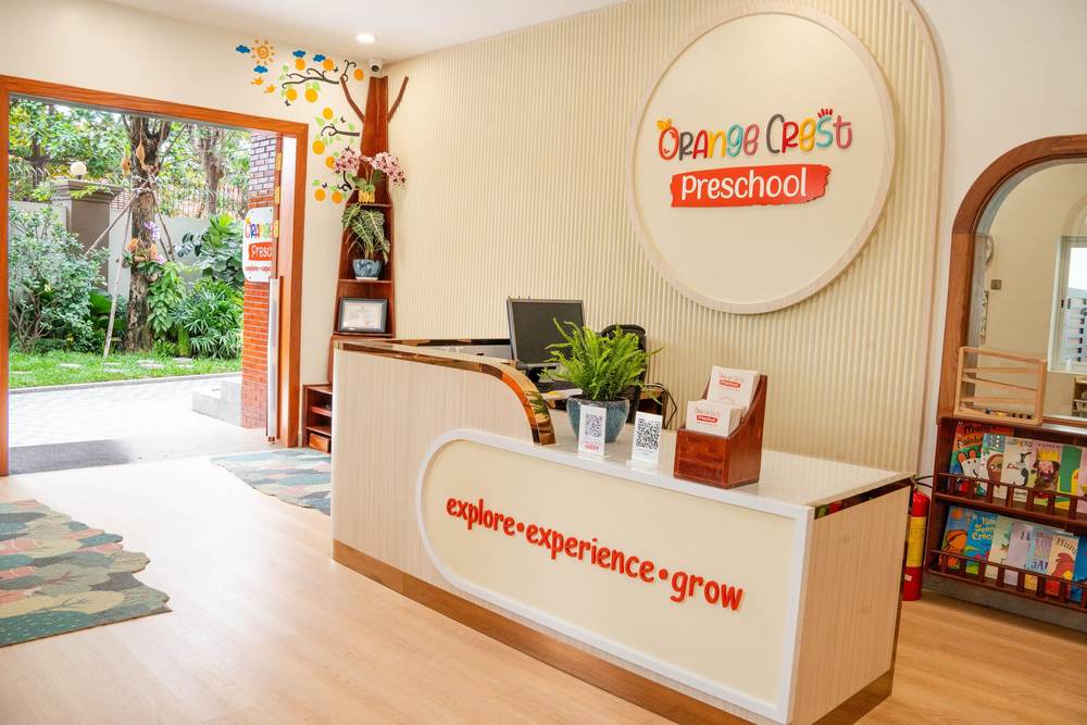 The reception desk at Orange Crest Preschool, with the round school sign on the wall behind it and the garden visible through the open door