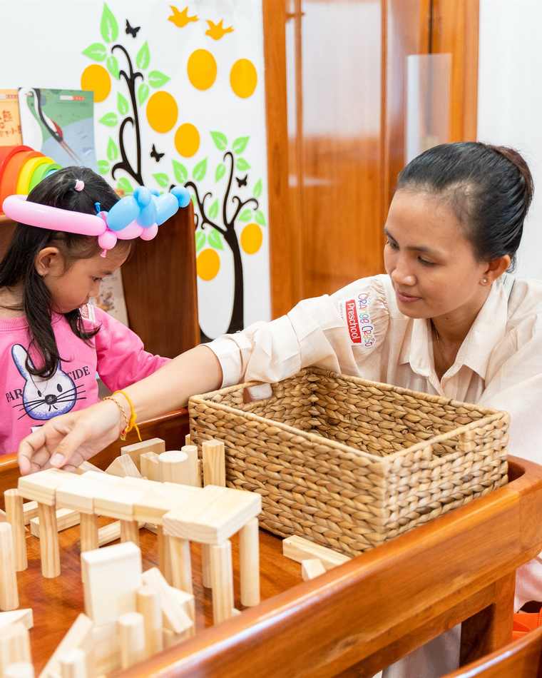 A teacher sitting with a child building with wooden blocks at Orange Crest Preschool