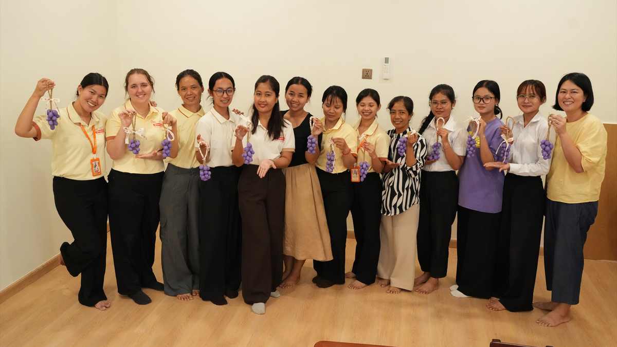 The Orange Crest Preschool teaching team standing together, each holding the bunch of grapes they made in the craft workshop