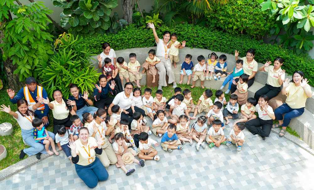 Children and teachers from Orange Crest Preschool sitting together in the garden, waving at the camera